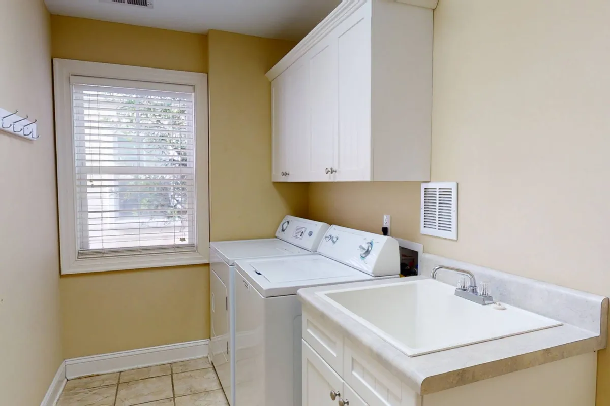 A tidy laundry room featuring a modern washing machine, dryer, and a utility sink under a window with blinds. The surfaces are clutter-free, and clean linens and towels are visible, emphasizing the home's focus on convenience and comfort.