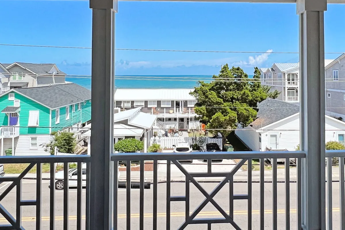 A welcoming living area offering a tranquil ocean view through large windows, with colorful houses and a green tree in the background. The space is designed for gathering and relaxation, perfectly illustrating the reverse floor plan's communal upper level.