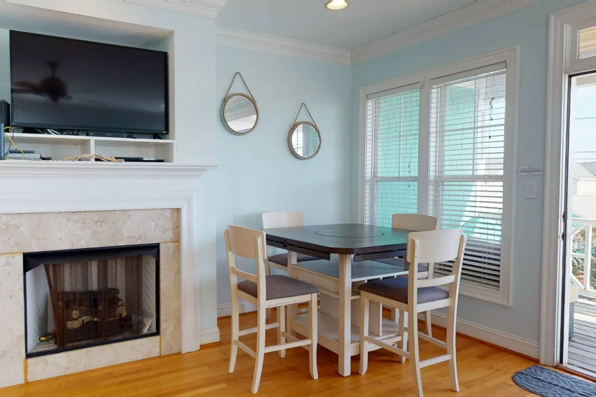 A cozy interior space with a fireplace, dining table, mirrors, and a TV. The room is bright, comfortable, and ideal for relaxing or spending time with loved ones (including pets) after a day by the sea.