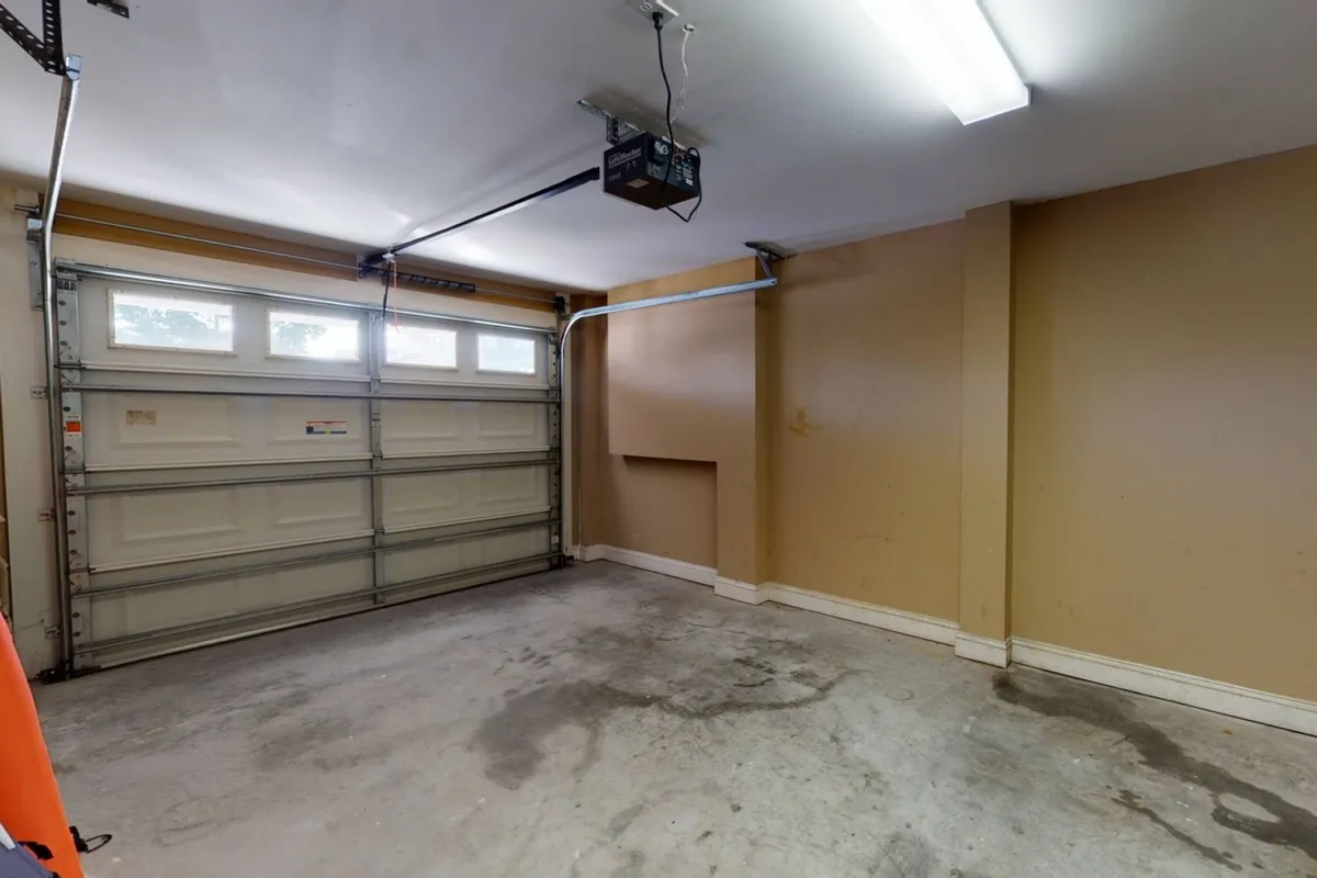 A functional garage space with a closed garage door, overhead lighting, and bare walls. The space is clean and organized, ideal for indoor parking or additional storage needs.
